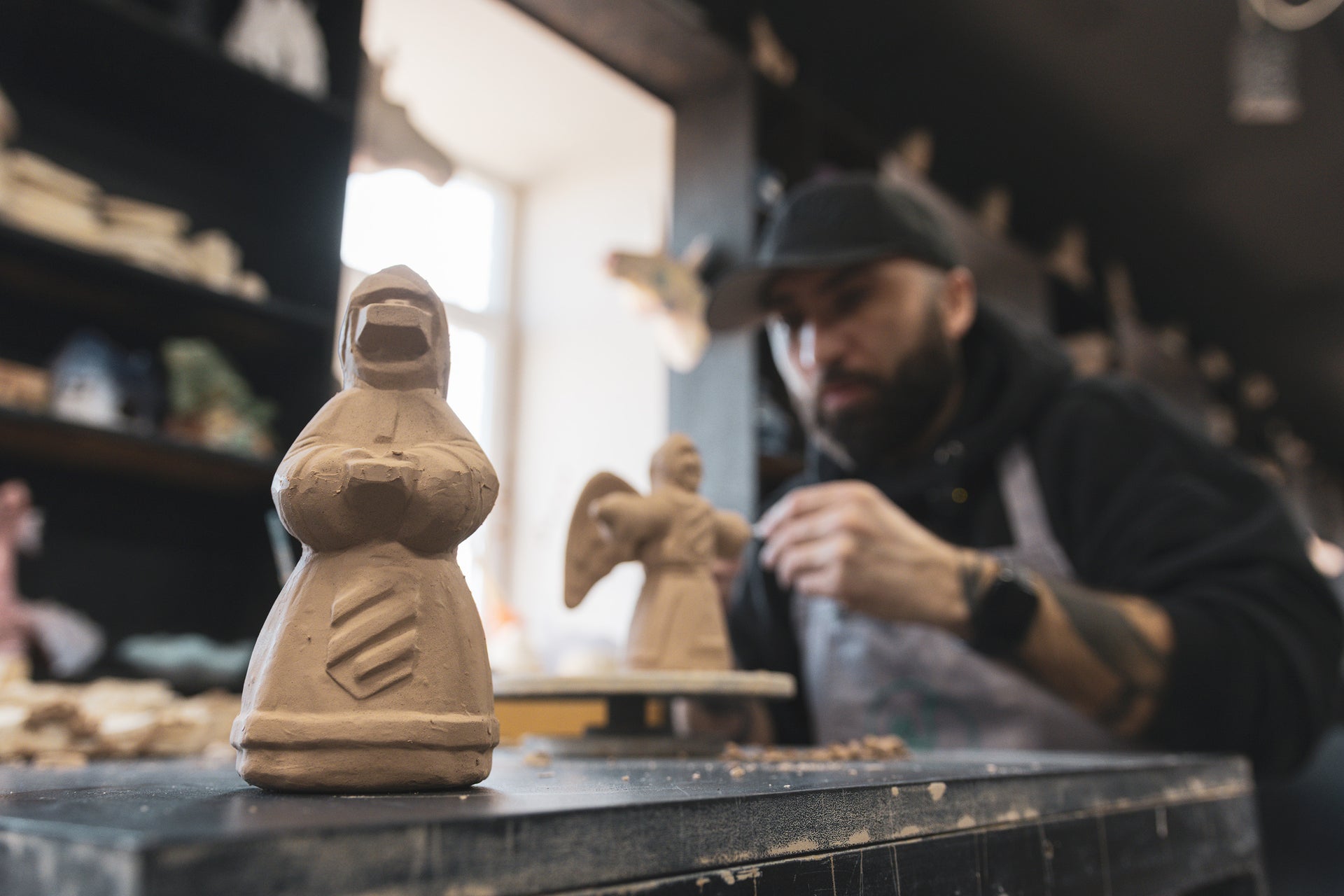Man working on a sculpture in a workshop with clay figures.