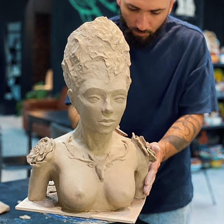Man working on a clay sculpture of a woman's bust in a workshop setting.