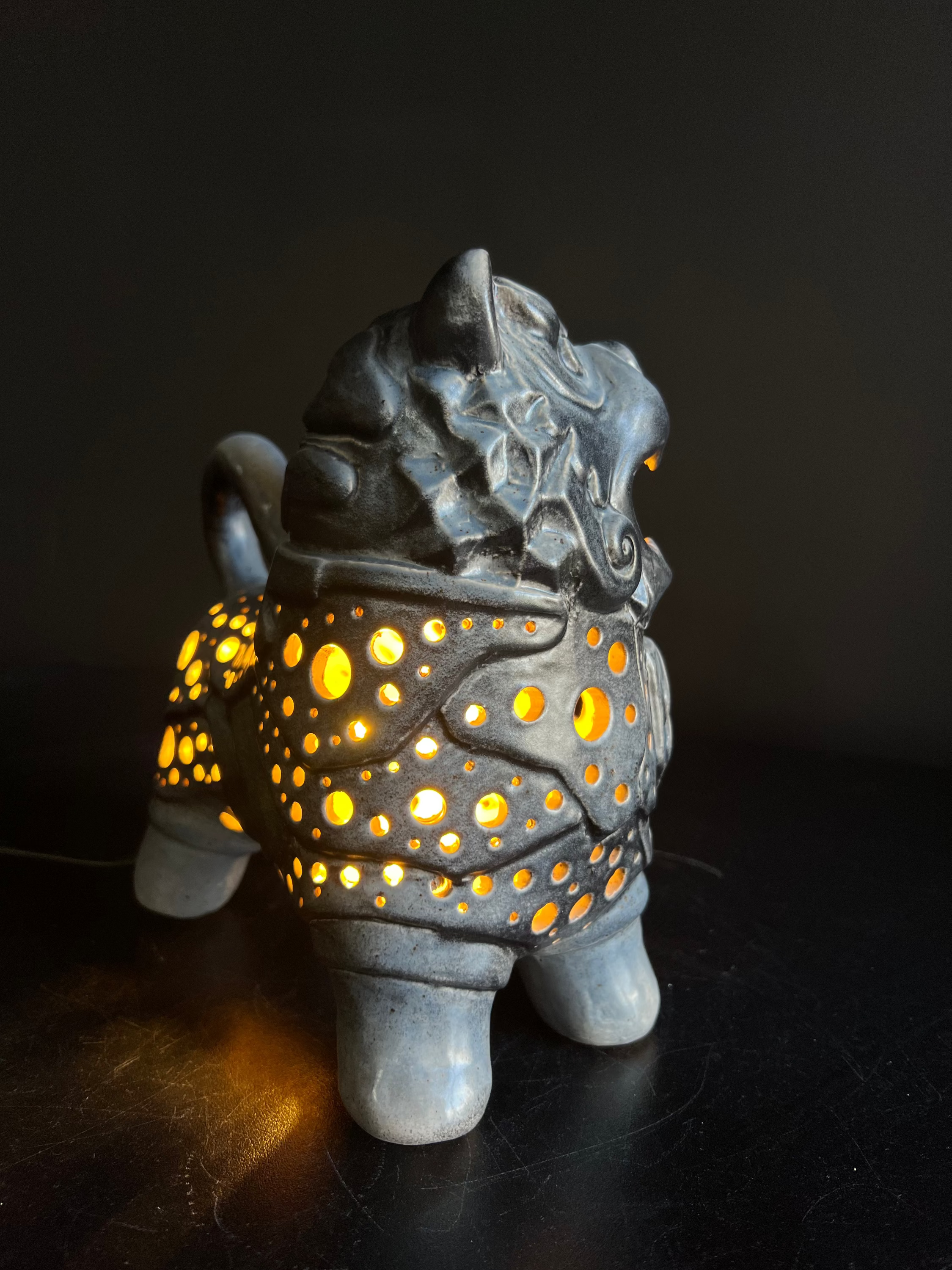 Ceramic lantern shaped like a mythical creature with glowing interior on a dark background