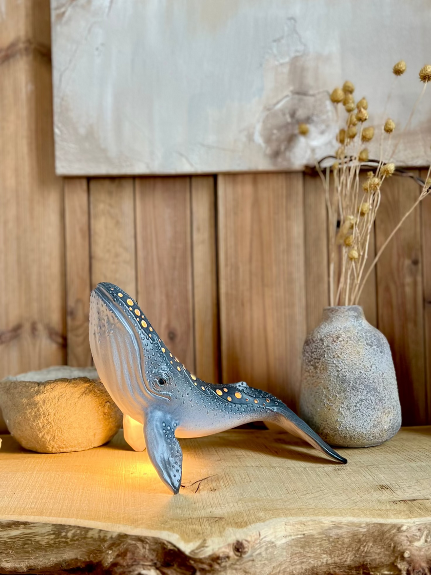 Decorative whale sculpture on a wooden surface with a vase and stones in the background.