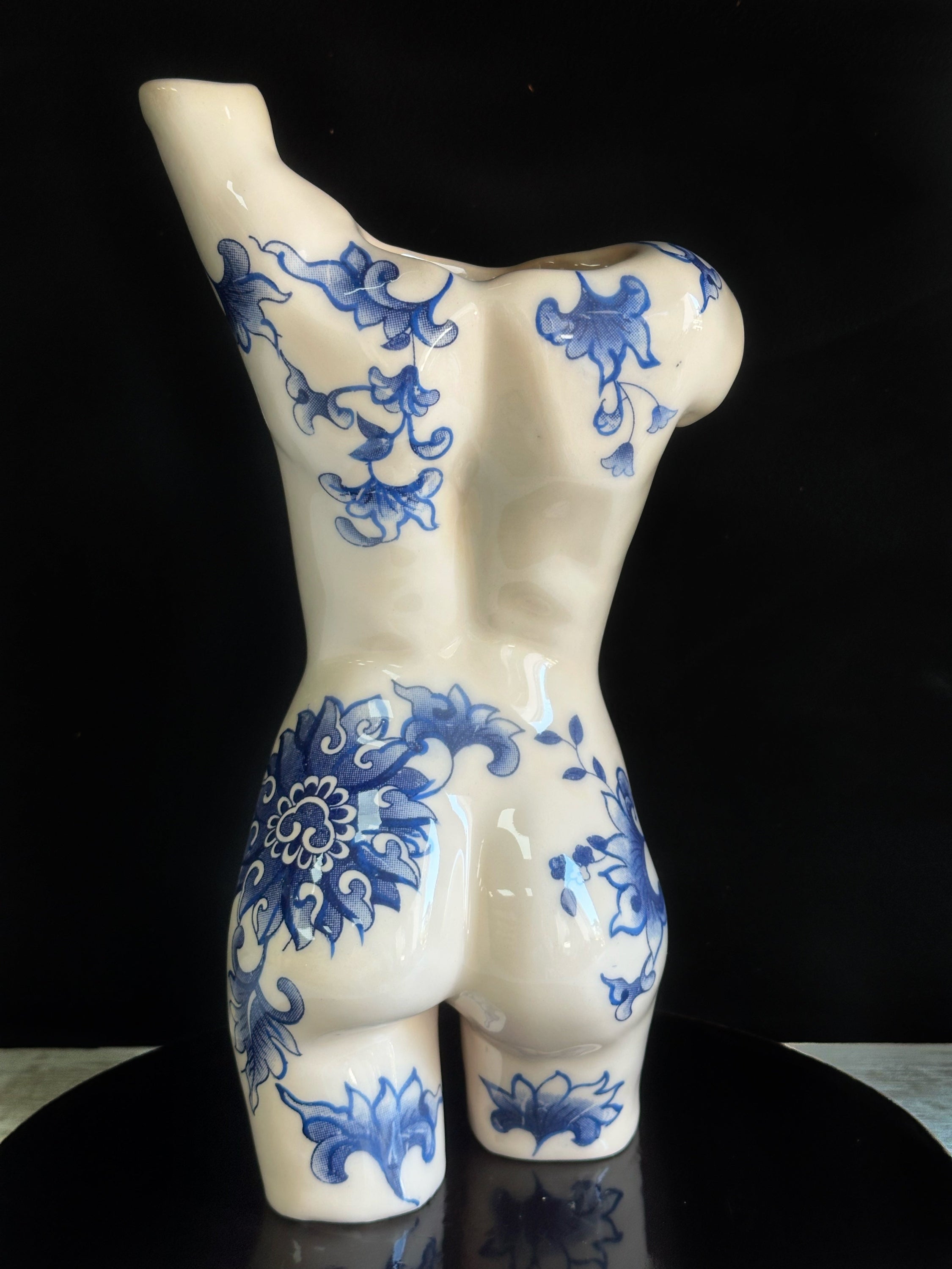 Ceramic vase shaped like a torso with blue floral patterns on a black background