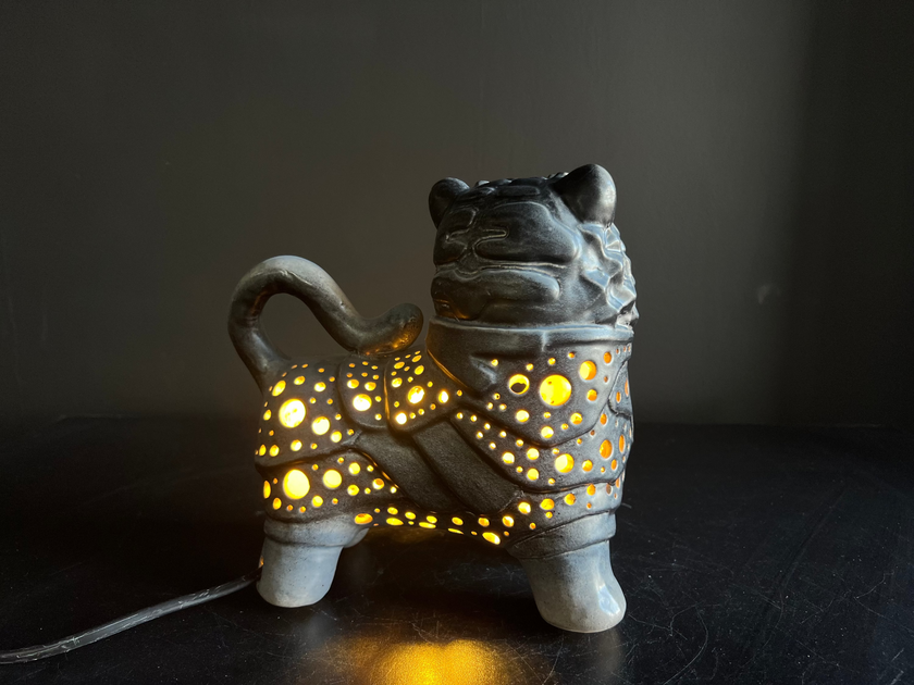 Ceramic lion-shaped lamp with glowing interior on a dark background