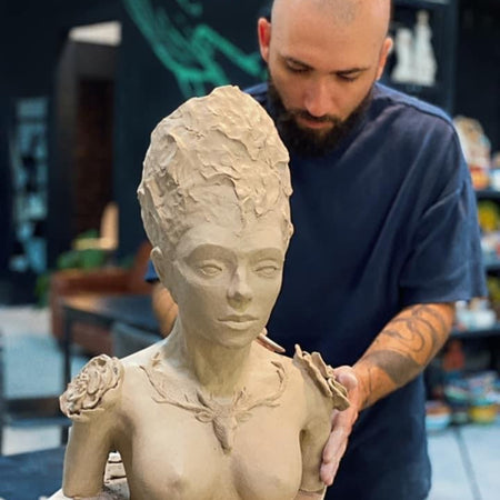 Man working on a clay sculpture of a woman's bust in a workshop setting.