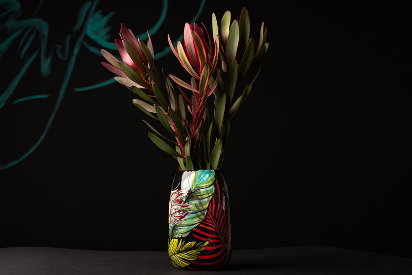 Decorative vase with colorful leaf design containing red and green leaves on a black background