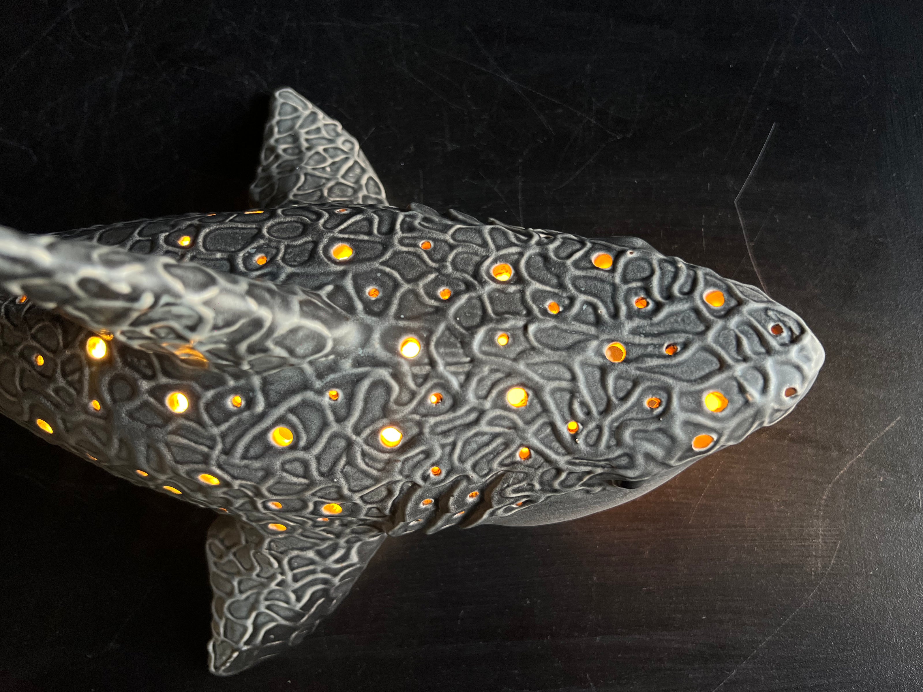 Decorative shark sculpture with textured surface and glowing orange spots on a dark background