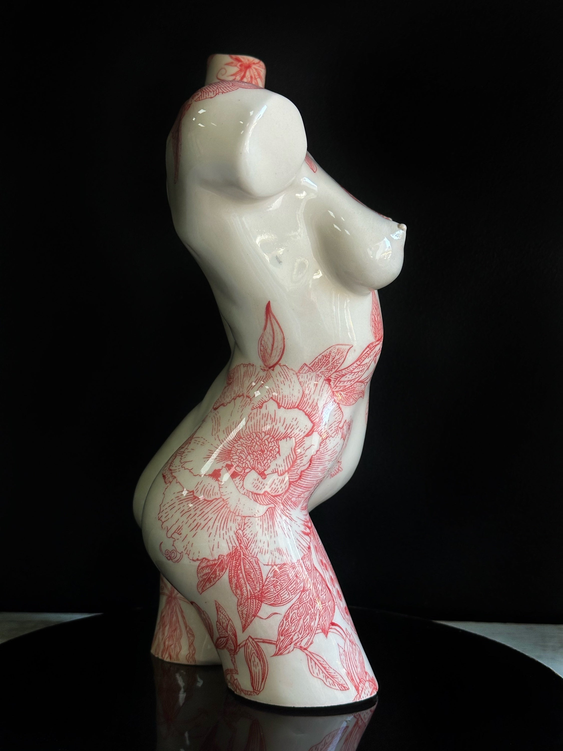 Ceramic vase shaped like a female torso with red floral patterns on a black background