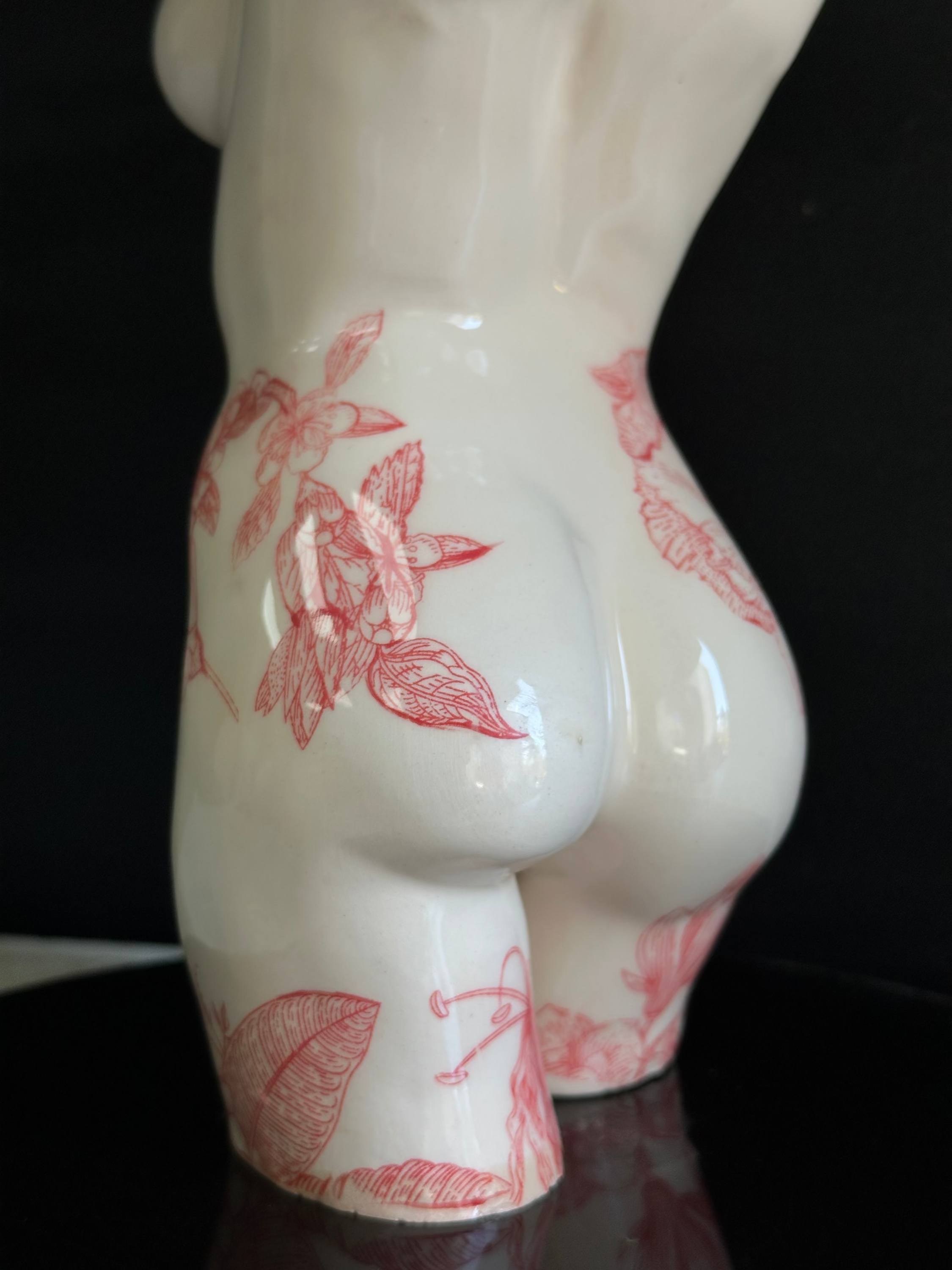 White ceramic figurine with red floral patterns on a black background