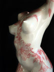 White ceramic figurine with red floral patterns on a black background