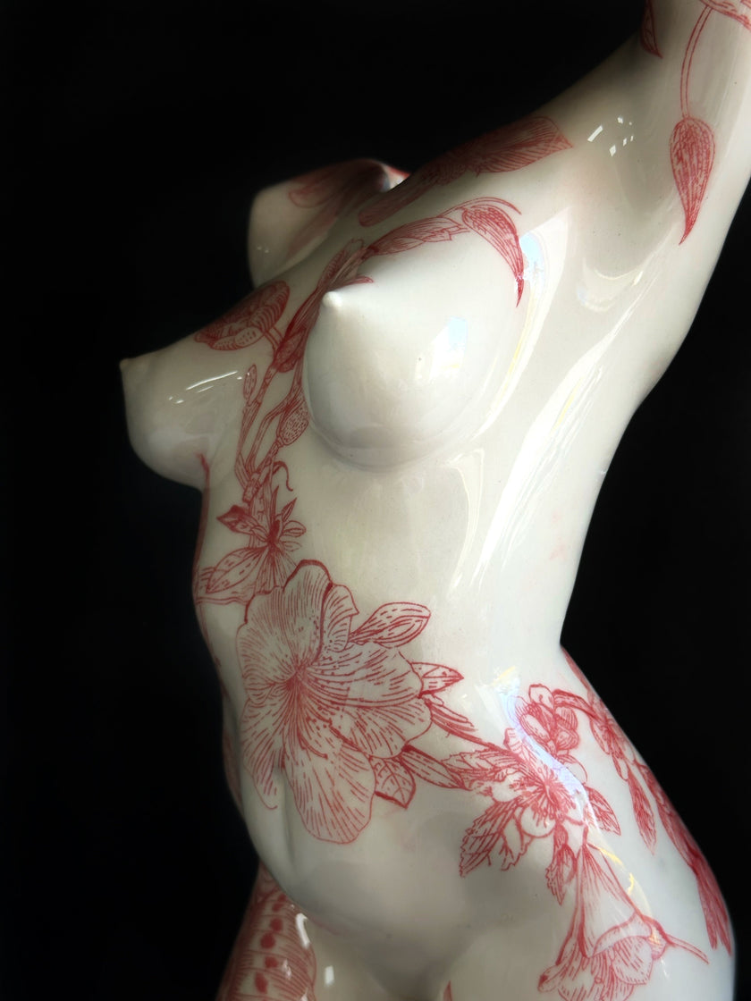 White ceramic figurine with red floral patterns on a black background